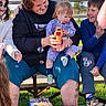 child, toddler, adult, outdoor, bench, bubble, bubble_gun, cotton_candy, face_paint, smiling, happy, grass, daylight, casual_clothing, family, fun, play, tattoo, people, blue_sky