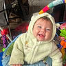 baby, child, smiling, onesie, hooded_clothing, indoor, toy, activity_center, playful, happy, face, hands, blue_eyes, colorful, infant, cute, plush, seated, young_child, warm_clothing