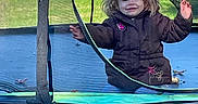 Oaklyn is registered to the contest to win money with this photo: brown_coat, casual, child, daylight, fun, grass, jacket, mesh_net, netting, outdoor, parked_car, person, play, playground, smiling, toy, trampoline, truck, vehicle, young_child