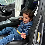 Shivan joined the competition — help win amazing prizes! child, toddler, car_interior, seat, black_leather, clothing, curly_hair, blue_outfit, hand, door, window, dashboard, armrest, seatbelt, young_child, person, automobile, modern, casual, playful
