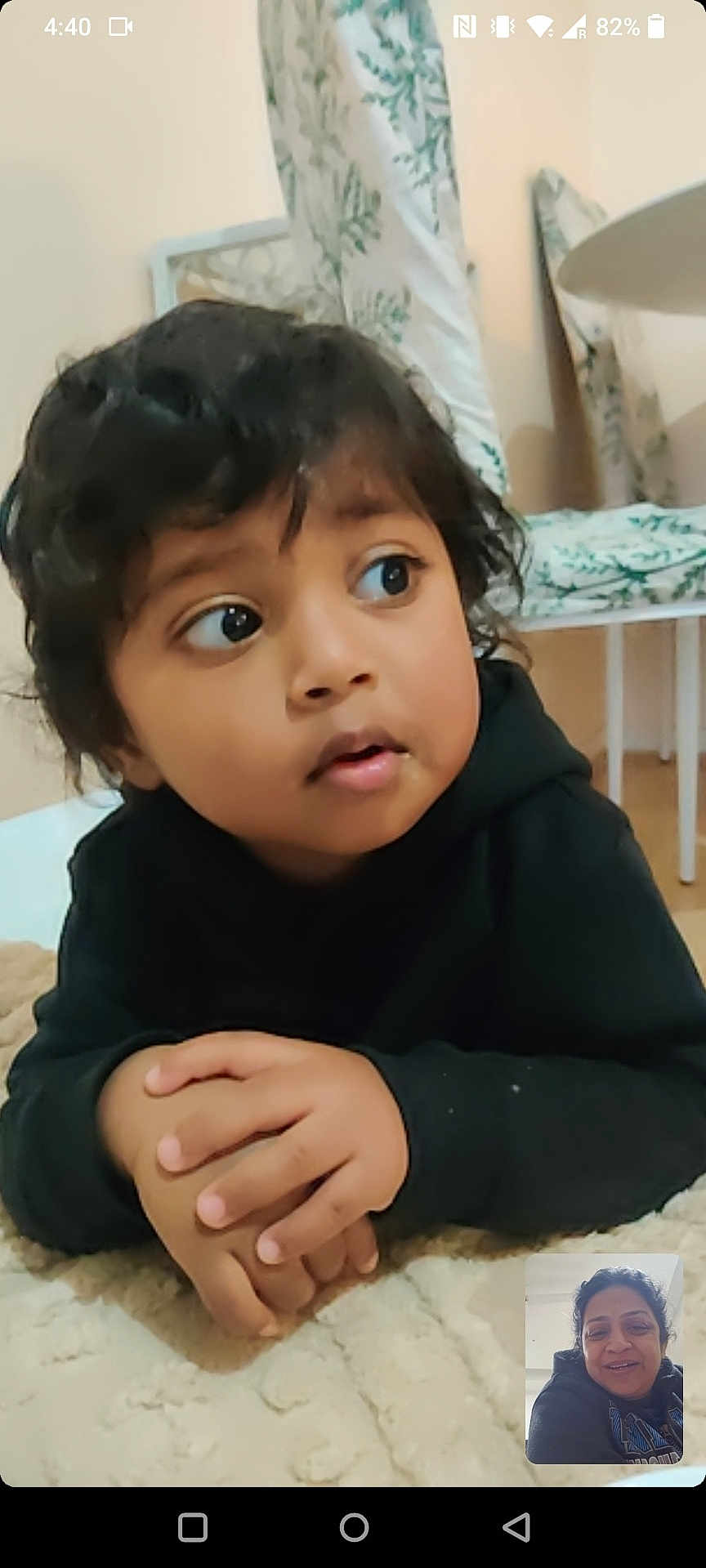 Riyansh a rejoint le concours — aidez-le/la à gagner de superbes lots ! child, toddler, hands, face, curly_hair, black_hoodie, indoor, blanket, video_call, adult, smile, person, furniture, table, curtain, home, expression, eyes, portrait, technology