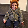 toddler, child, smiling, jacket, hat, bear_ears, sitting, indoor, couch, footwear, happy, cute, warm_clothing, person, portrait, cozy, baby, face, expression, home