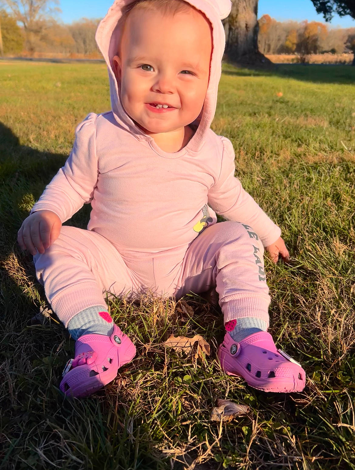 Kinsley is registered to the contest to win money with this photo: baby_toddler_clothing, eye, finger, grass, happy, iris, joy, leaf, light, morning, people_in_nature, person, photograph, pink, plant, skin, sky, sleeve, smile, sunlight