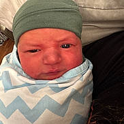 Tristian joined the competition — help win amazing prizes! baby, newborn, infant, swaddle, blanket, beanie, hat, face, eyes, cheeks, portrait, close_up, cozy, indoor, pillow, bedding, person, skin, expression, caretaker