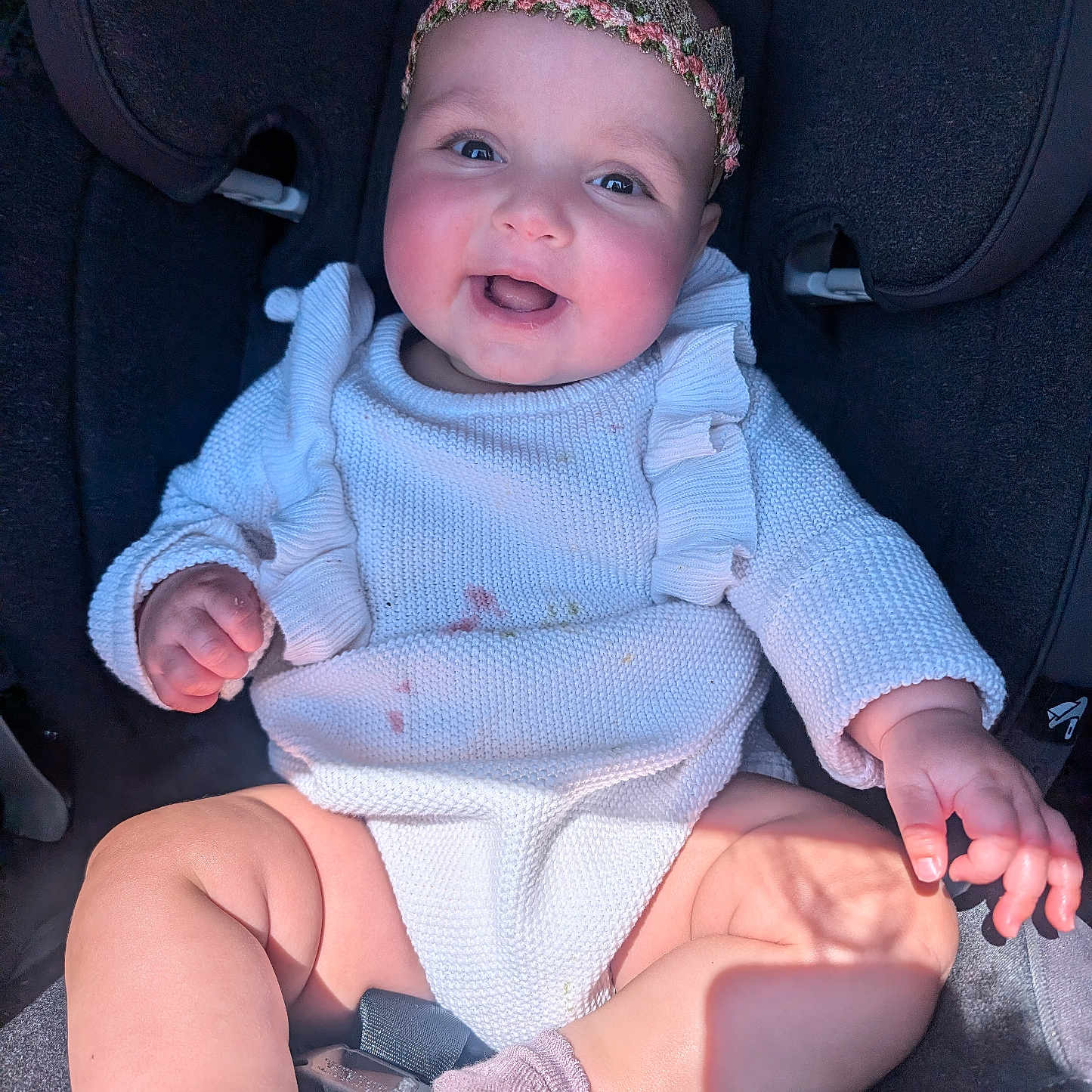 Dahlia is registered to the contest to win money with this photo: baby, car_seat, child, closeup, clothing, cute, happy, headband, indoors, infant, knitted_clothing, person, pink_socks, portrait, rosy_cheeks, shadow, sitting, smiling, sunlight, young_child