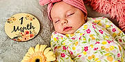 Sofia joined the competition — help win amazing prizes! baby, sleeping, headband, flower, blanket, pink, gray, onesie, floral_pattern, soft_texture, infant, cute, peaceful, wooden_plaque, age_marker, portrait, closeup, indoor, newborn, resting