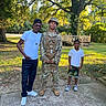 Dewayne is registered to the contest to win money with this photo: child, boy, adult, soldier, military_uniform, family, group_portrait, outdoor, backyard, trees, sunlight, wooden_deck, grass, concrete, smiling, standing, camouflage, baseball_cap, white_shirt, sneakers