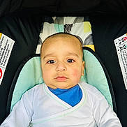 Azlan is registered to the contest to win money with this photo: baby, child, infant, car_seat, seat, clothing, white_shirt, blue_shirt, face, head, eyes, expression, indoor, seatbelt, fabric, pattern, cute, person, portrait, young