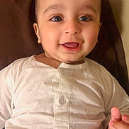 Azlan Malik is registered to the contest to win money with this photo: baby, child, smile, happy, face, eyes, white_clothing, cushion, brown_background, infant, portrait, cute, lying_down, indoors, skin, hand, young_child, person, closeup, head