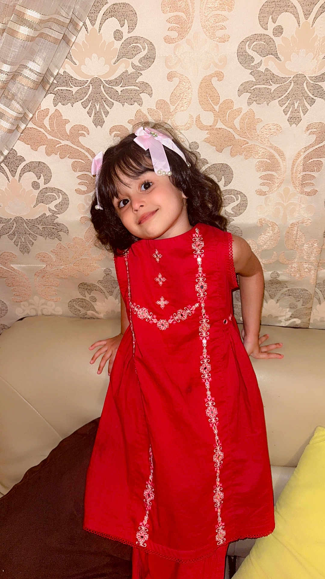 Aakifa is registered to the contest to win money with this photo: child, girl, red_dress, smile, ribbons, hair_accessory, couch, indoor, patterned_wallpaper, cheerful, portrait, cute, playful, home_interior, seated, young_child, decor, furniture, curtain, happy