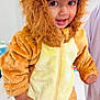 Viyaan is registered to the contest to win money with this photo: animal_costume, baby, child, costume, curly_hair, cute, face, foot, fur, hand, hood, indoors, lion_costume, person, plush, smiling, standing, supporting_hand, toddler, zipper