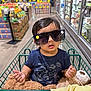 accessory, aisle, baby, blanket, casual, child, clothing, cute, expression, funny, grocery_store, indoor, person, plush_toy, portrait, retail, shopping, shopping_cart, sunglasses, toddler