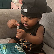 Zaccai is registered to the contest to win money with this photo: toddler, child, baby, cap, black_clothing, chain, toy, baby_wipes, couch, indoor, foot, skin, face, hand, sitting, curious, furniture, relaxed, home, casual