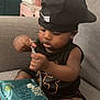 toddler, child, baby, cap, black_clothing, chain, toy, baby_wipes, couch, indoor, foot, skin, face, hand, sitting, curious, furniture, relaxed, home, casual