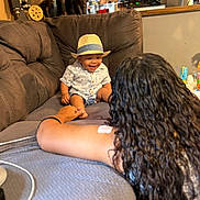 Lataivean is registered to the contest to win money with this photo: toddler, child, hat, couch, smile, person, long_hair, living_room, kitchen, wood_paneling, home_interior, furniture, interaction, happy, casual_clothing, playful, indoor, family, bonding, cozy