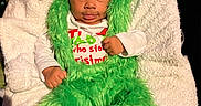 Lataivean is registered to the contest to win money with this photo: baby, child, green_fur, hat, costume, christmas, holiday, blanket, white, plush, cute, funny_expression, tongue_out, indoor, festive, person, clothing, seated, smile, decorations