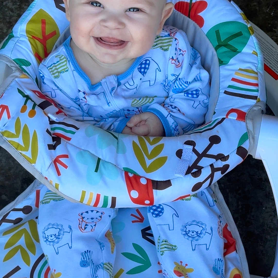 Stetson is registered to the contest to win money with this photo: animal_print, baby, baby_seat, child, clothing, colorful, comfort, cute, face, footed_pajamas, happy, indoors, infant, joy, pajamas, patterned, portrait, sitting, smiling, young