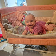 Leela joined the competition — help win amazing prizes! baby, playpen, pink_outfit, smiling, soft_toys, indoor, child, face, happy, home, floor, blanket, person, infant, furniture, cushion, portrait, toddler, toy, room