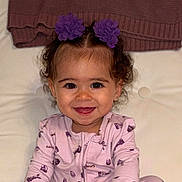 Legaci is registered to the contest to win money with this photo: toddler, child, smiling, purple_flower, hair_clip, curly_hair, pink_onesie, sitting, indoor, blanket, happy, face, portrait, baby, cute, infant, apparel, person, cozy, background