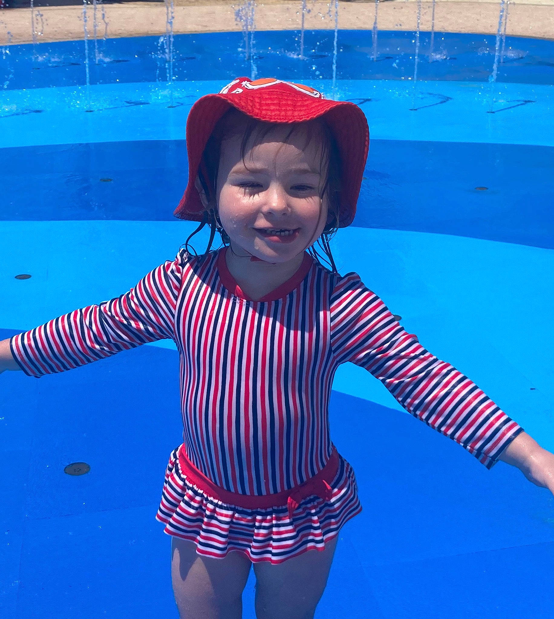 Lilith is registered to the contest to win money with this photo: azure, blue, cool, gesture, happy, hat, headgear, human_body, joy, line, organ, outerwear, person, pink, red, shoulder, sleeve, smile, standing, wall