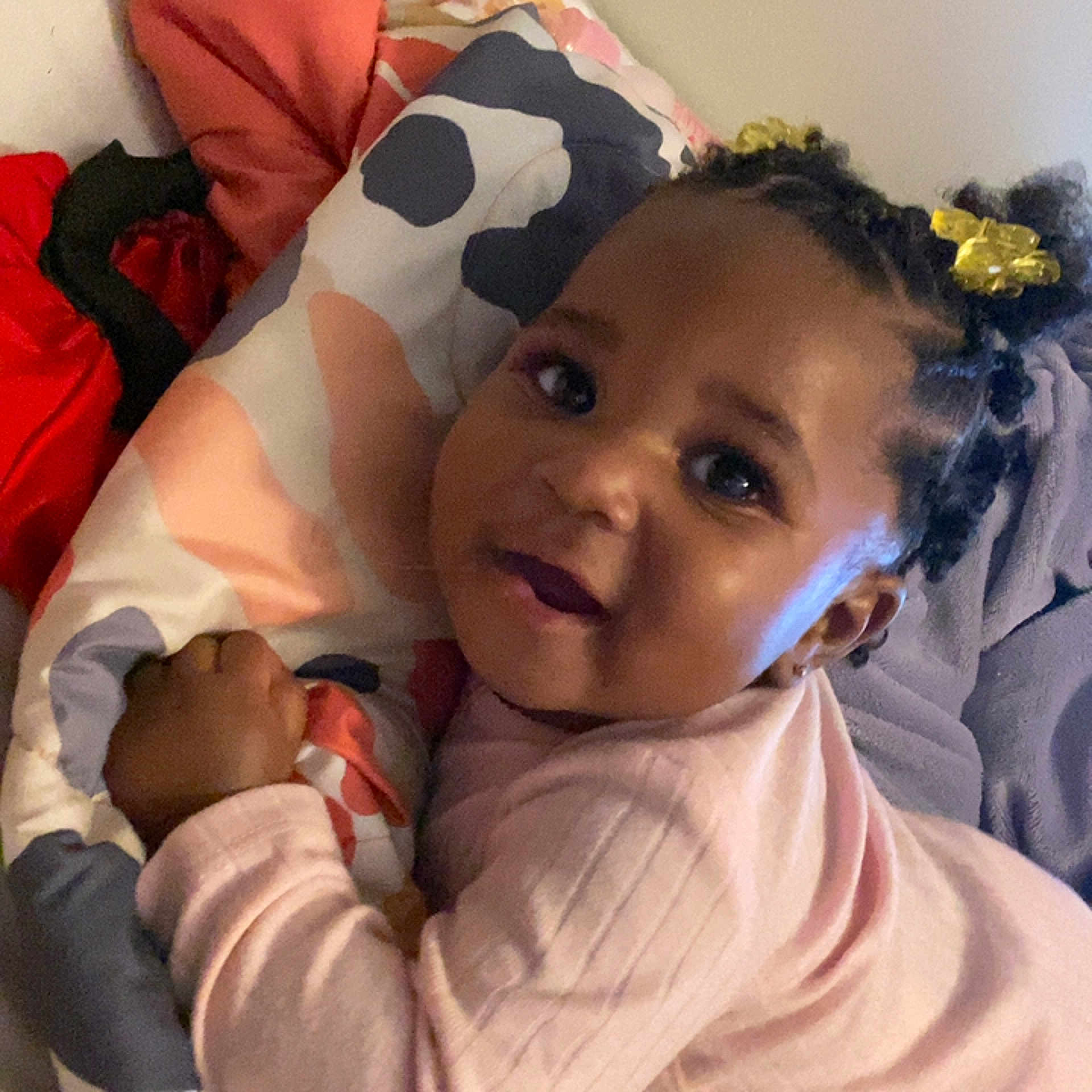 Londyn joined the competition — help win amazing prizes! toddler, child, smiling, face, braided_hair, yellow_hair_clips, pink_clothing, pillow, blanket, indoor, cute, portrait, baby, cozy, resting, person, closeup, expression, young_child, lying_down