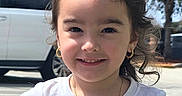 Brianna is registered to the contest to win money with this photo: child, girl, smile, white_tshirt, heart_design, gold_necklace, gold_hoop_earrings, white_bow, hair_accessory, outdoor, sunny_day, trees, vehicle, sidewalk, person, portrait, casual_clothing, happy, cute, curly_hair