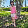Brianna is registered to the contest to win money with this photo: child, girl, sunglasses, pink_top, shorts, purse, tree, grass, outdoor, sunny, sidewalk, shoes, greenery, summer, casual, playful, fashion, accessory, nature, daytime