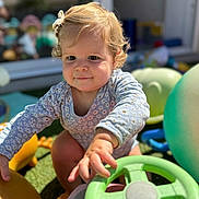 Olympe participe au concours pour gagner de l'argent avec cette photo : toddler, child, baby, outdoor, toy, steering_wheel, grass, sunlight, play, cute, curly_hair, onesie, hand, face, expression, daylight, garden, fun, colorful, young_child