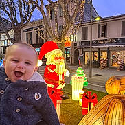Owen a rejoint le concours — aidez-le/la à gagner de superbes lots ! baby, child, smiling, holiday_lights, christmas_decorations, santa_claus, gift_boxes, illuminated_animals, outdoor, trees, festive, night, street, winter_clothing, person, celebration, holiday, joy, warm_coat, twinkling_lights