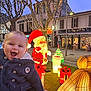 baby, child, smiling, holiday_lights, christmas_decorations, santa_claus, gift_boxes, illuminated_animals, outdoor, trees, festive, night, street, winter_clothing, person, celebration, holiday, joy, warm_coat, twinkling_lights