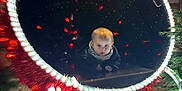 Owen participe au concours pour gagner de l'argent avec cette photo : baby, child, face, lights, night, outdoor, festive, circular_frame, glowing, red_lights, white_lights, curious, portrait, decorations, holiday, tree, dark_background, young_child, winter_clothing, photography