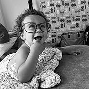 Bentley joined the competition — help win amazing prizes! toddler, child, glasses, blanket, couch, smiling, curly_hair, indoor, happy, portrait, hand, furniture, bag, patterned_curtain, black_and_white, cozy, cute, relaxed, playful, infant