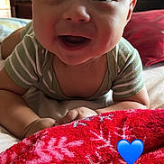 Alexander is registered to the contest to win money with this photo: baby, child, smiling, face, tummy, bed, blanket, red_blanket, snowflake_pattern, onesie, striped_clothing, happy, indoors, closeup, human, infant, cute, portrait, blue_heart_emoji, cozy