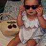 toddler, child, sunglasses, red_sunglasses, white_outfit, cherry_pattern, bag, straw_bag, bed, pillow, indoor, cute, fashion, sitting, barefoot, person, portrait, young_child, hair_tied, playful