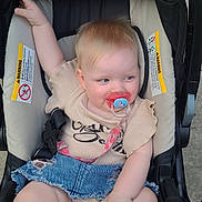 Janet is registered to the contest to win money with this photo: baby, stroller, pacifier, child, denim_skirt, beige_top, sitting, cute, infant, outdoor, safety_straps, happy, smiling, skin, hair, footwear, one_arm_raised, comfort, childcare, playful