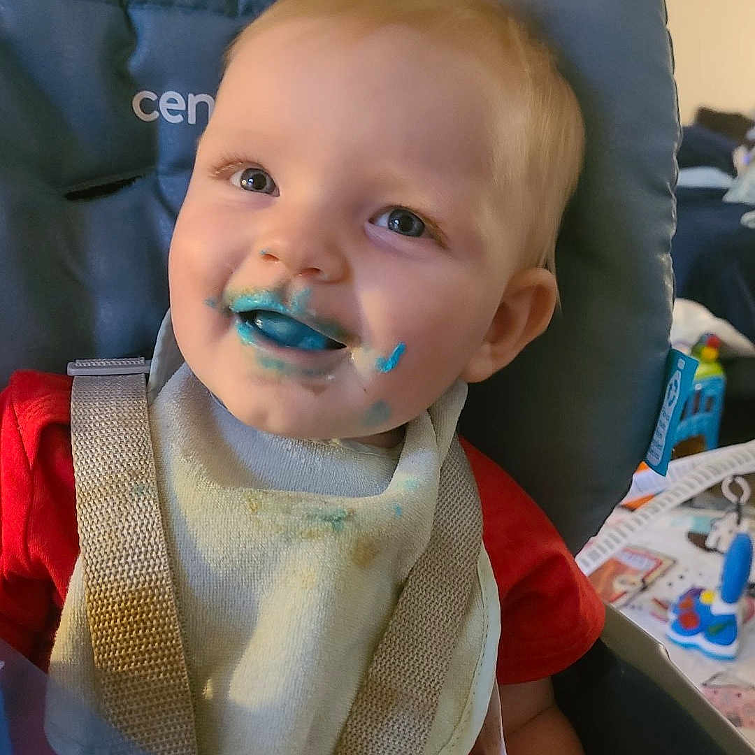 Janet is registered to the contest to win money with this photo: baby, bib, blue_food, child, cute, face, feeding_time, food_stains, happy, high_chair, indoor, messy, playful, portrait, red_shirt, seat, smile, straps, toddler, young_child