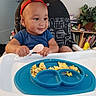 baby, high_chair, spoon, food, scrambled_eggs, plate, reindeer_antlers, child, smiling, indoor, furniture, plant, books, toy_duck, blue_shirt, feeding_time, happy, face, person, home