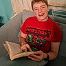 child, boy, smiling, portrait, indoor, sitting, couch, book, reading, minecraft, red_shirt, short_hair, happy, face, person, home, curtains, radiator, casual_clothing, photography