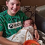 child, baby, smiling, sleeping, blanket, plate, food, bagel, couch, pillow, indoor, radiator, person, happy, holding, clothing, green_shirt, home, family, portrait