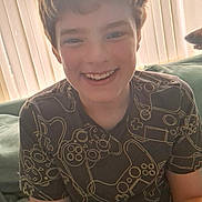 James joined the competition — help win amazing prizes! child, boy, smile, happy, tshirt, video_game_controller_pattern, couch, blanket, indoors, face, hair, portrait, casual, relaxed, window_blinds, light, person, seated, young, home