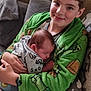 child, baby, smiling, sleeping, green_hoodie, couch, cushion, indoors, family, sibling, comfortable, cozy, portrait, person, holding, clothing, happy, face, home, relaxation