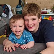James is registered to the contest to win money with this photo: toddler, child, sibling, smiling, indoor, living_room, couch, boy, happy, casual, family, portrait, face, hair, clothing, toy, background, person, young, candid