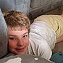 child, smile, face, white_shirt, yellow_shorts, couch, cushion, carpet, indoor, relaxed, happy, young, person, resting, lying_down, home, casual, comfortable, short_hair, closeup