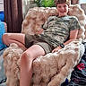 blanket, boy, camo_clothing, chair, child, curtain, face, furniture, happy, home, indoor, legs, person, plant, relaxed, shorts, smile, tshirt, watch, window