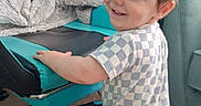 Orlando joined the competition — help win amazing prizes! toddler, child, smiling, checkered_clothing, gaming_chair, blanket, indoor, carpet, furniture, person, baby, happy, standing, blue, black, technology, monitor, cozy, home, cute