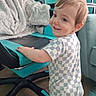 toddler, child, smiling, checkered_clothing, gaming_chair, blanket, indoor, carpet, furniture, person, baby, happy, standing, blue, black, technology, monitor, cozy, home, cute