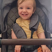 Orlando is registered to the contest to win money with this photo: toddler, child, smile, stroller, seatbelt, yellow_shirt, orange_shorts, happy, baby, quilted_seat, gray_stroller, person, infant, casual_clothing, indoor, portrait, young_child, seat, hands, face