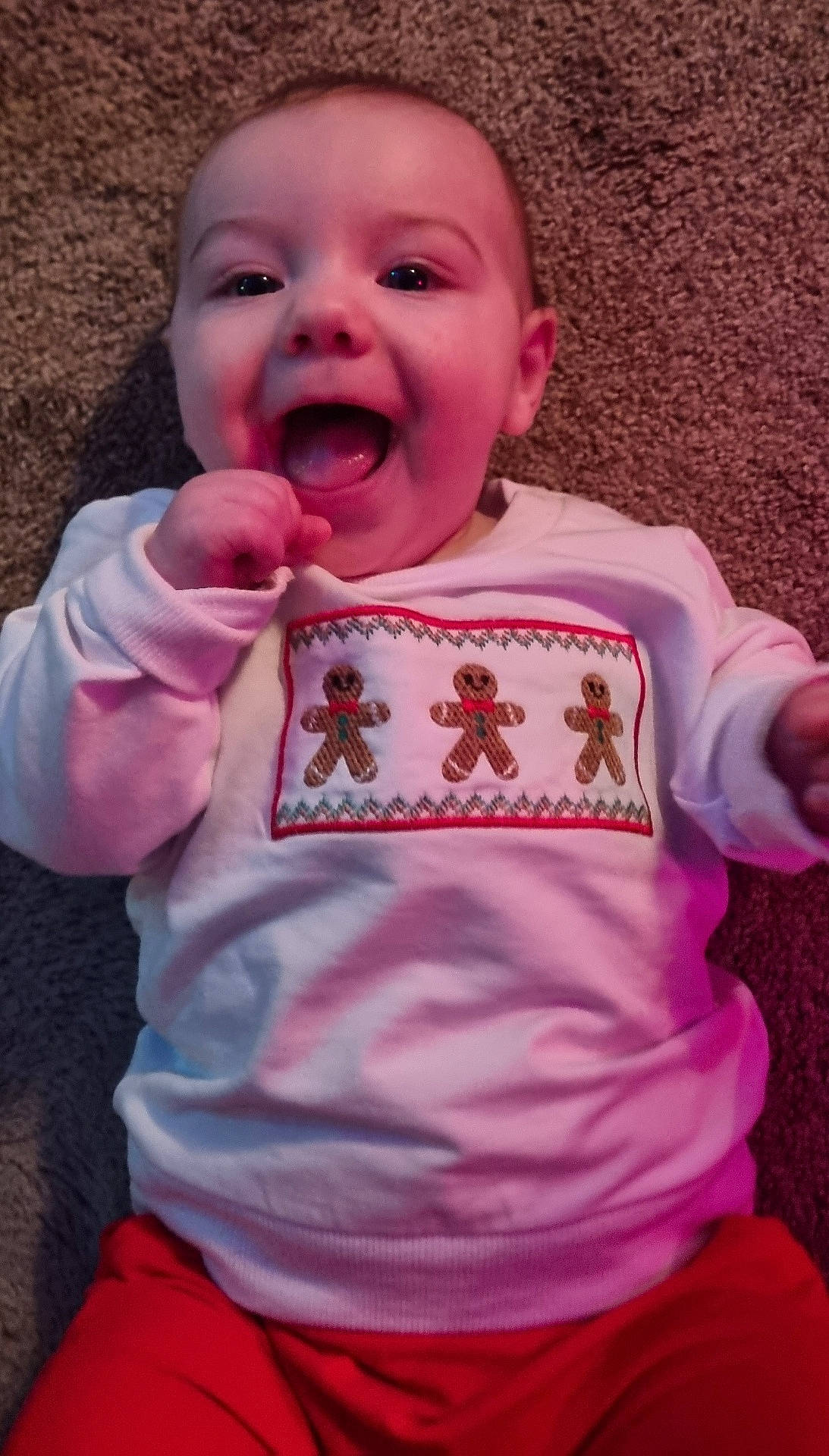 Orlando is registered to the contest to win money with this photo: baby, carpet, cheerful, child, close_up, clothing, cute, face, gingerbread_men, hand, happy, indoors, infant, joyful, lying_down, portrait, red_pants, smiling, sweater, toddler