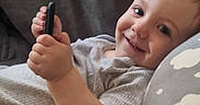 Orlando is registered to the contest to win money with this photo: baby, child, clothing, couch, cute, face, gray, hand, happy, holding, home, indoors, infant, person, pillow, portrait, relaxed, small_object, smiling, young_child