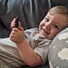 baby, child, clothing, couch, cute, face, gray, hand, happy, holding, home, indoors, infant, person, pillow, portrait, relaxed, small_object, smiling, young_child